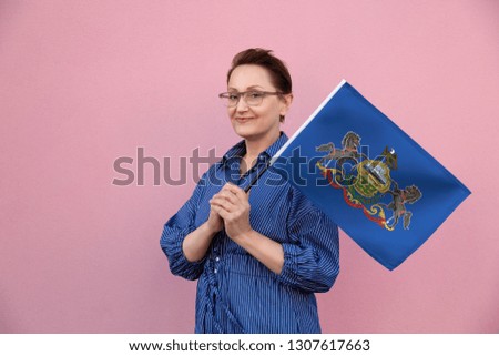 Pennsylvania flag. Woman holding Pennsylvania state flag. Nice portrait of middle aged lady 40 50 years old holding a large state flag over pink wall background on the street outdoor.