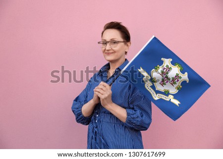 Connecticut flag. Woman holding Connecticut state flag. Nice portrait of middle aged lady 40 50 years old holding a large state flag over pink wall background on the street outdoor.