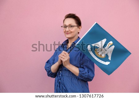 Louisiana flag. Woman holding Louisiana state flag. Nice portrait of middle aged lady 40 50 years old holding a large state flag over pink wall background on the street outdoor.