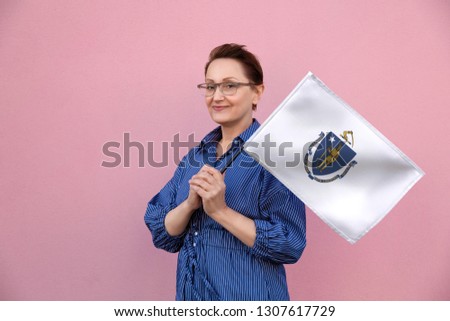 Massachusetts flag. Woman holding Massachusetts state flag. Nice portrait of middle aged lady 40 50 years old holding a large state flag over pink wall background on the street outdoor.
