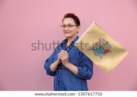 New Jersey flag. Woman holding New Jersey state flag. Nice portrait of middle aged lady 40 50 years old holding a large state flag over pink wall background on the street outdoor.