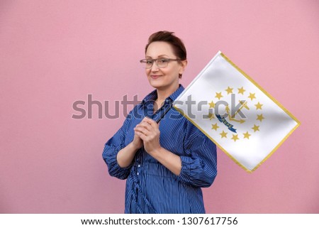 Rhode Island flag. Woman holding Rhode Island state flag. Nice portrait of middle aged lady 40 50 years old holding a large state flag over pink wall background on the street outdoor.