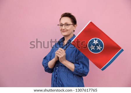 Tennessee flag. Woman holding Tennessee state flag. Nice portrait of middle aged lady 40 50 years old holding a large state flag over pink wall background on the street outdoor.