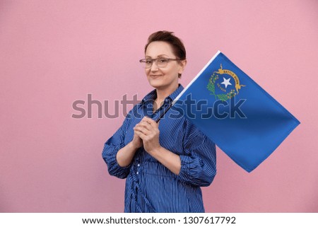 Nevada flag. Woman holding Nevada state flag. Nice portrait of middle aged lady 40 50 years old holding a large state flag over pink wall background on the street outdoor.