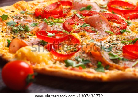 Close up Italian pizza with ham, cheese, pepper and herbs on a brown table decorated by mushrooms, red sweet pepper and cherry tomatoes