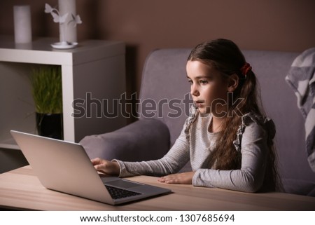 Cute little girl with laptop watching cartoons in evening