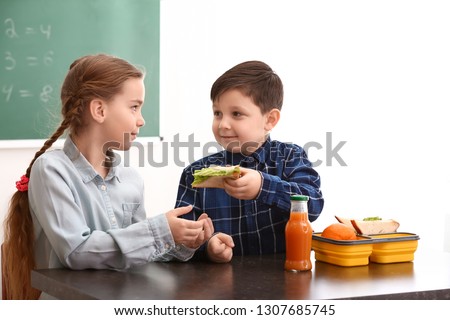 Little boy sharing his school lunch with girl in classroom Royalty-Free Stock Photo #1307685745