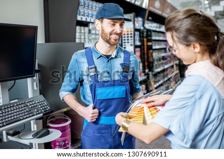 Young woman client choosing paint from color swatches, standing with workman in supermarket with building goods