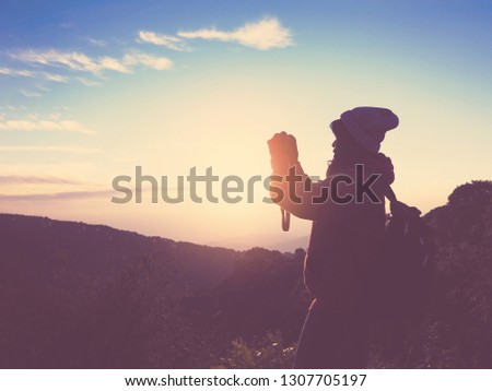Asian tourist woman standing on mountain and taking natural landscape photograph at sunrise with blue sky background. Weekend vacation concept. Vintage filter effect