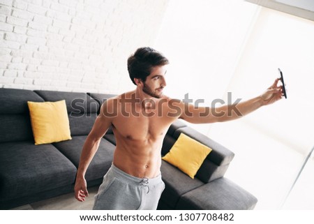 Young bare chested man training and working out at home. Handsome hispanic male athlete after a routine of exercise, taking a selfie picture or video with mobile phone for his blog.