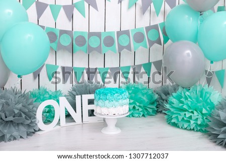 Photo zone with paper garlands, balloons, paper balls, pom poms, confetti and cream cake. Birthday cake. Smash cake. One year. Mint, white, grey colors. 