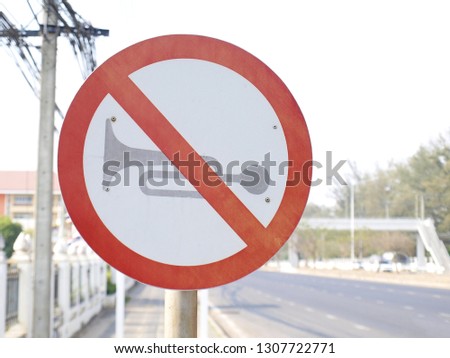 Close up do not use vehicles horn sign stick on pole Sign stick horns on the street signs in the streets near hospitals and schools. There is a concrete road background and blurred white sky.