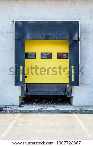 Front view of a truck loading bay with rubber seals in the concrete wall of a warehouse in the suburbs of Paris, France, with a closed yellow roller shutter door.