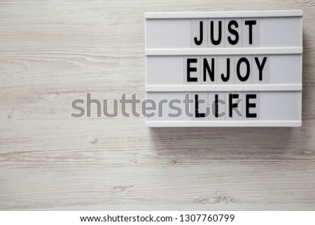 Modern board with text 'Just enjoy life' on a white wooden surface, top view. Copy space.