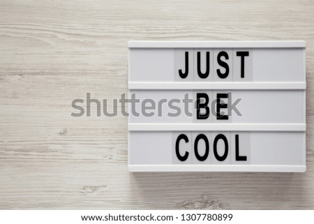 Modern board with text 'Just be cool' on a white wooden table, top view. From above, flat lay, overhead. Space for text.