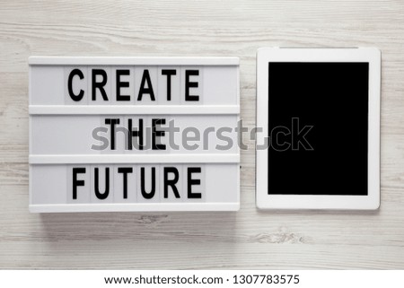 Modern board with text 'Create the future', tablet on a white wooden surface, top view. From above, flat lay, overhead. 