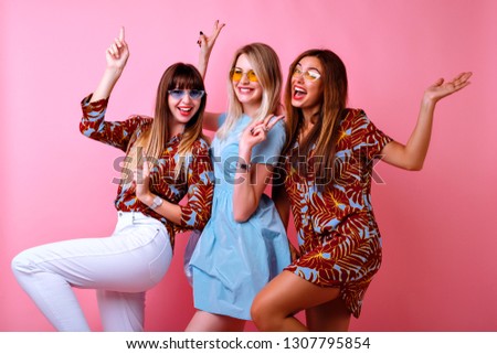 Crazy funny picture of three happy best friends girls enjoying party time together, dancing and laughing, color matching trendy elegant outfits and glasses, positive mood, pink background.
