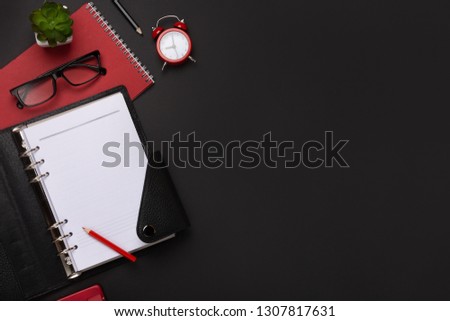 Black background red coffee cup notepad alarm clock flower diary scores keyboard on the table.  
