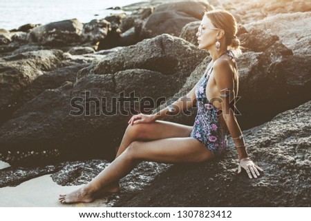 Photo of beautiful boho styled model wearing ethnic swimwear and silver bohemian jewelery on the beach in sunset