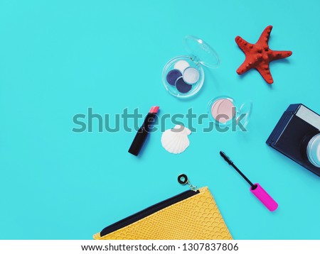 Yellow cosmetic bag, lipstick, mascara, seashells on a blue background. Summer makeup concept. Flat lay beauty photo