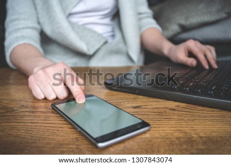 Close up cropped photo of unrecognizable lady sitting inside loft interior space in restaurant. She touching portable telephone equipment with copy space on display and using laptop
