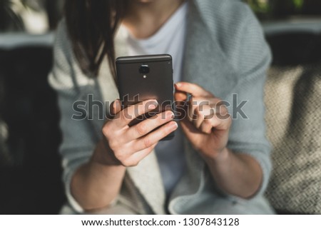 Close up and cropped photo of unrecognizable lady with portable telephone equipment in hands. She sitting inside loft interior space in restaurant and pointer on display