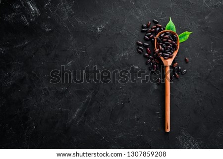 Raw beans in a wooden spoon on a black background. Top view. Free copy space.