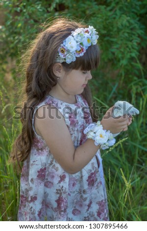 
Easter theme with a little girl with a wreath on her head in the garden with bunnies in her hands
