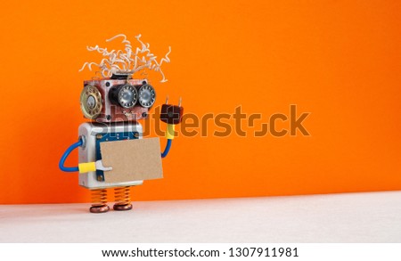 Funny robot with a cardboard card mockup. Creative design robotic toy holding a blank and empty paper poster, orange wall background. copy space for text and design elements.
