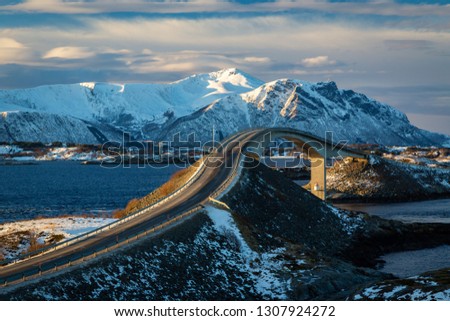 Atlantic Ocean Road - Atlanterhavsvegen in winter sunny day. Famous high bridge over the sea called Storseisundbrua and beautiful snowy mountains in a horizon. Royalty-Free Stock Photo #1307924272