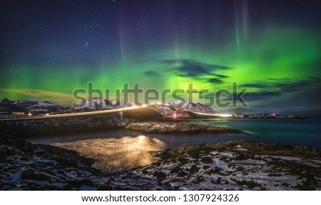 Amazing night sky with Aurora Borealis over Atlantic Ocean Road in Norway. View on the famous bridge and lights from running car. Royalty-Free Stock Photo #1307924326