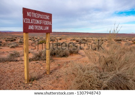 No trespassing - Violation of federal and tribal law - warning brown road sign with white lettering on the wooden post in desert landscape, overcast during day time