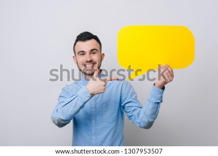 Handsome young student is holding a yellow speech bubble, pointing on it and smiling