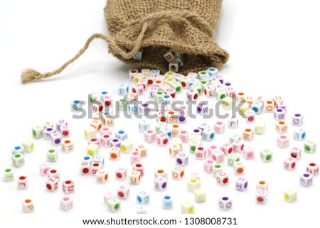 Colorful English alphabet cube beads spilling out of hemp bag scattered on white background with copy space