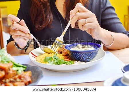 Long hair no face woman enjoy eating Thai food at restaurant, crop picture focus at plate of food, hands holding spoon and fork pick crumble egg in dish, blue bowl of sticky rice, happy meal concept