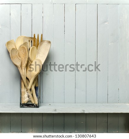 Wooden cooking utensils on shelf; good copy-space; photographed against rustic wall; add your own text to the blank spine of the 'cookery book'
