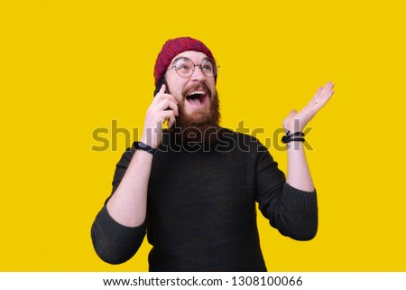 Portrait of a handsome young bearded man in white sweater talking on mobile phone isolated over yellow background