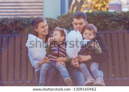 Natural pictures of a happy family of four having fun outsiade  and eating sugar floss. A family of four on a sunny autumn day. Togetherness and happiness concept