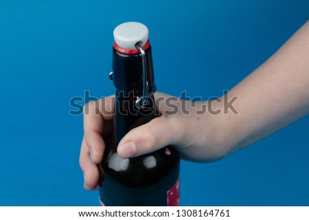 A picture of a bottle of beer in a young persons hand showing mainly the top of the bottle and the rubber seal