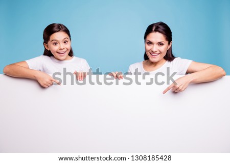 Close up photo beautiful two people brown haired mom little daughter finger point on signboard poster arms hold white poster sale discount wearing t-shirts isolated bright blue background