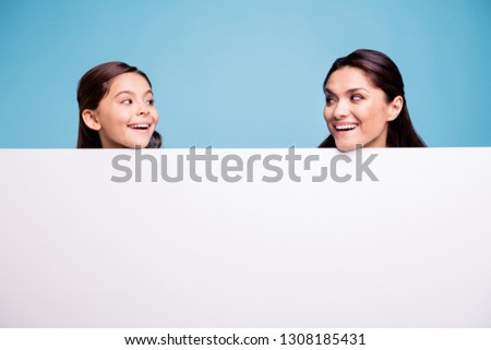 Close up photo beautiful two people brown haired mom little daughter amazing look at each other signboard poster gladly open mouth laugh laughter wearing t-shirts isolated bright blue background