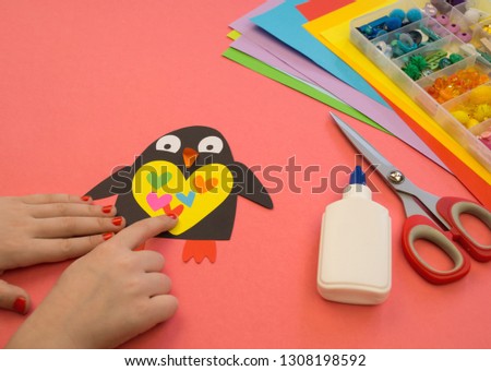 Penguin made of paper on a pink background. Workshop. Children's hands glue crafts. Kindergarten and school. Favorite hobby.