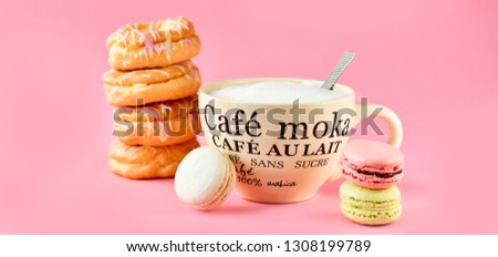 a large Cup of cappuccino coffee and donuts and a lot of colorful  French macarons, on the Cup inscription in French (mocha coffee, coffee with milk). pink background, selective focus