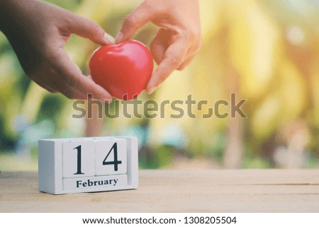 close up wooden calendar on old wood table, hand holding red heart background, 14 february text, countdown to holiday season, happy valentine's day concept, vintage tone
