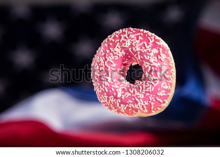Sweet pink icing donut isolated over waving american flag, unusual minimal