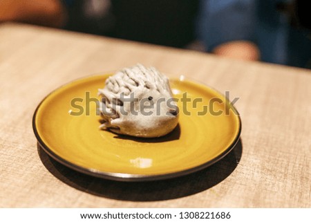Porcupine shaped black bean bao. Served in yellow ceramic plate.