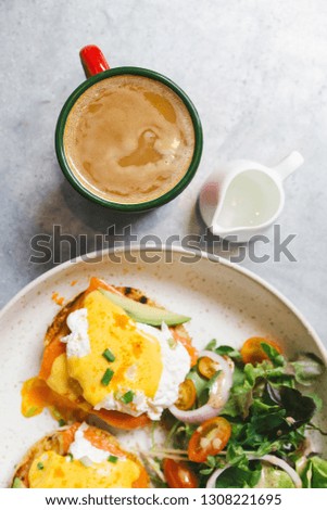 Top view of Egg Benedict with salmon and avocado, Served with salad in white plate. Served with hot coffee and milk.