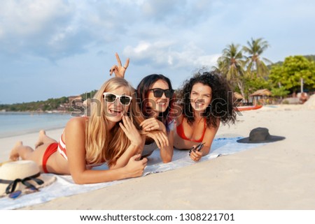 Three young beautiful girlfriends in bikini relaxing on a tropical beach, travel and vacation concept