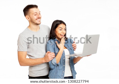 Closeup photo of young couple looking at laptop and pointing on the screen, happy and smiling, wearing casual street wear, isolated on white background