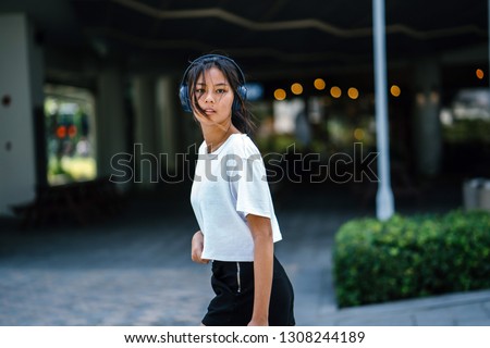 Portrait of a beautiful, young and elegant Chinese Asian millennial teenage girl dancing and walking as she listens to music on her headphones that she is streaming on her smartphone. 
